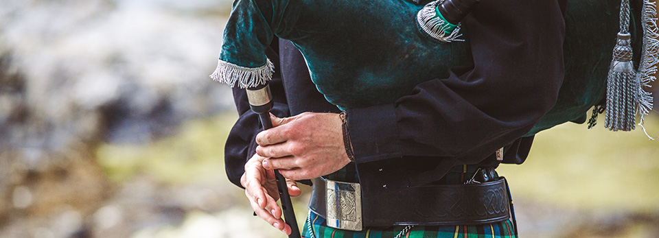 Bagpipe A close-up view of a bagpiper in traditional Scottish Highland dress, holding the chanter of a green velvet bagpipe.
