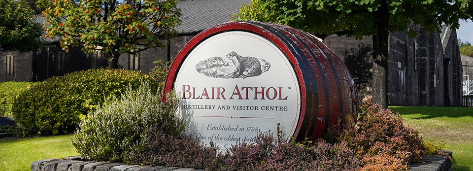 Blair-Athol A large wooden whisky barrel head framed by plants serving as the entrance sign for the Blair Athol Distillery and Visitor Centre.