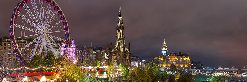 Edinburgh A vibrant night view of Edinburgh featuring a lit-up Ferris wheel, illuminated historic monuments, and city lights.