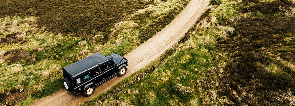 Land-Rover High-angle top-down view of a black Land Rover driving along a winding dirt path through green and brown moorland.